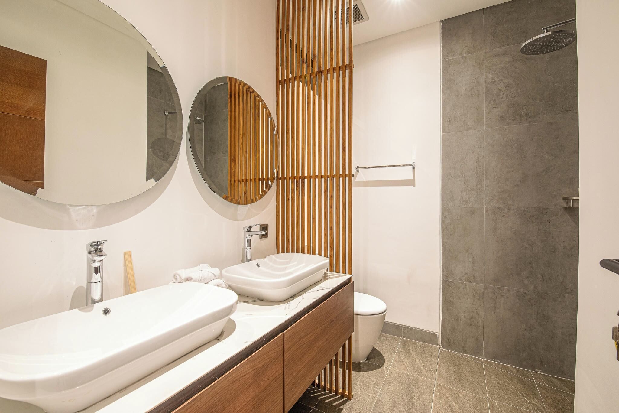 Une salle de bain moderne avec un meuble-lavabo en bois, deux vasques, des toilettes et une douche.