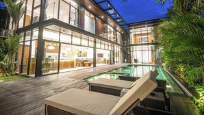 A modern house with a glass facade, a pool, and outdoor seating. - Elegant 6BR Canggu Villa Steps From the Ocean (Seminyak)