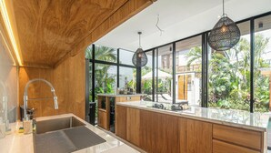 Una cucina moderna con mobili in legno, un lavello in acciaio inossidabile e ampie finestre che danno su un giardino tropicale.