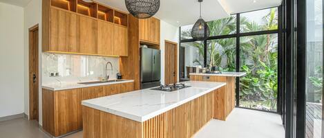 Une cuisine moderne avec des meubles en bois, un grand îlot central et des luminaires suspendus.
