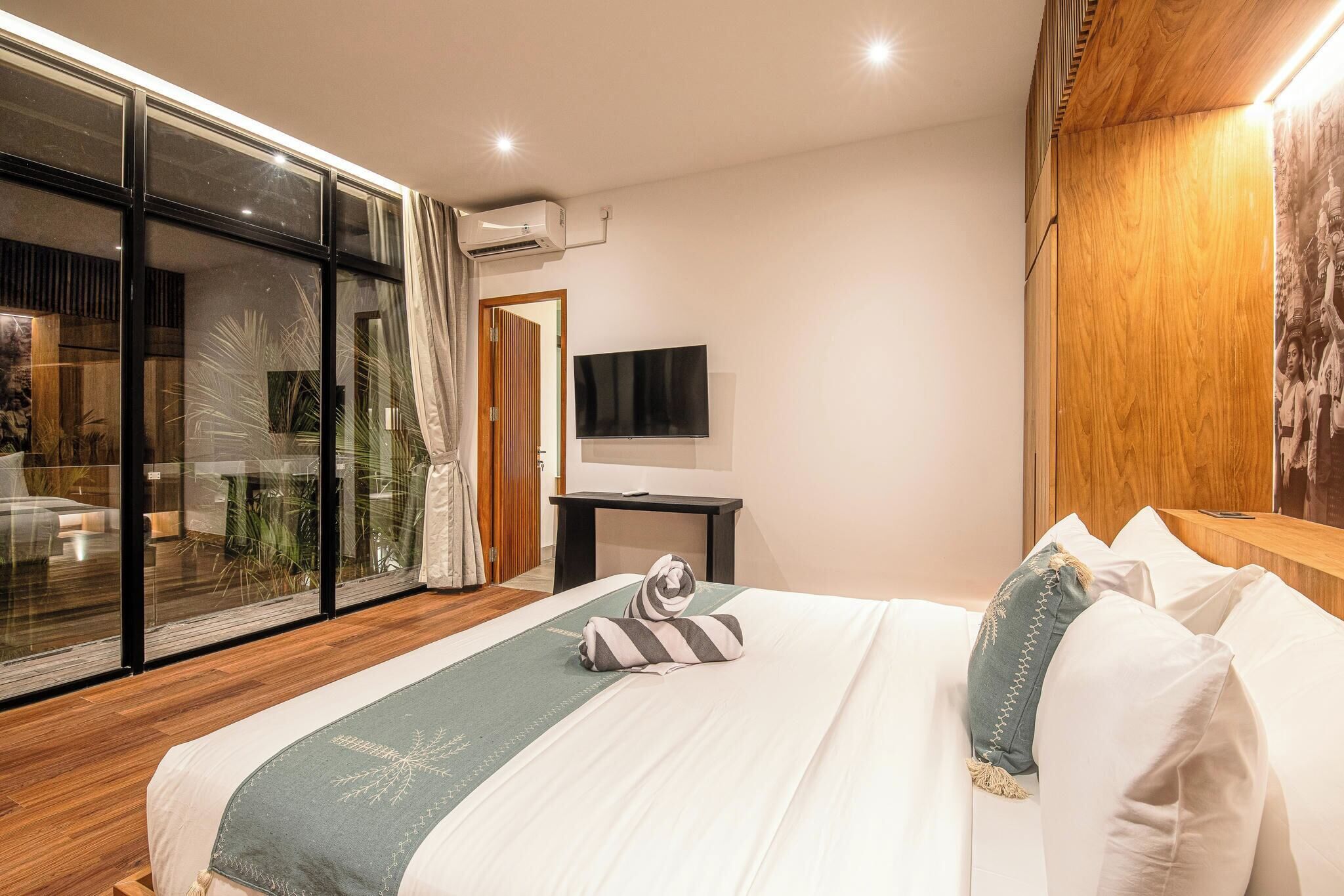 Ein modernes Hotelzimmer mit einem großen Bett, einem Flachbildfernseher und einer Glasschiebetür, die auf einen Balkon führt.
