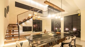 A modern dining area with a large marble table, six chairs, a wooden staircase, and a hanging light fixture. - Elegant 4BR Seminyak Villa 10min From the Shore (Seminyak)
