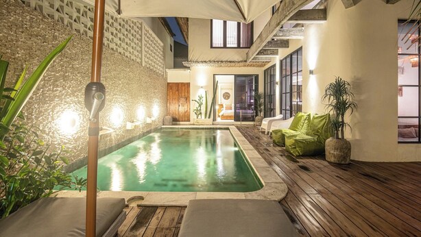 A pool area with a wooden deck, lounge chairs, and a wall with a textured pattern. - Elegant 4BR Seminyak Villa 10min From the Shore (Seminyak)
