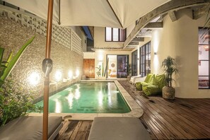 Un área de piscina con cubierta de madera, sillas de descanso y una pared con diseño texturizado.