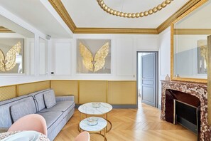 A room with a grey sofa, two round tables with decorative items, a fireplace, and golden wall decorations. - Superb AC- 1BDR Ave Montaigne - Arc de Triomphe by Studio Prestige (Paris)