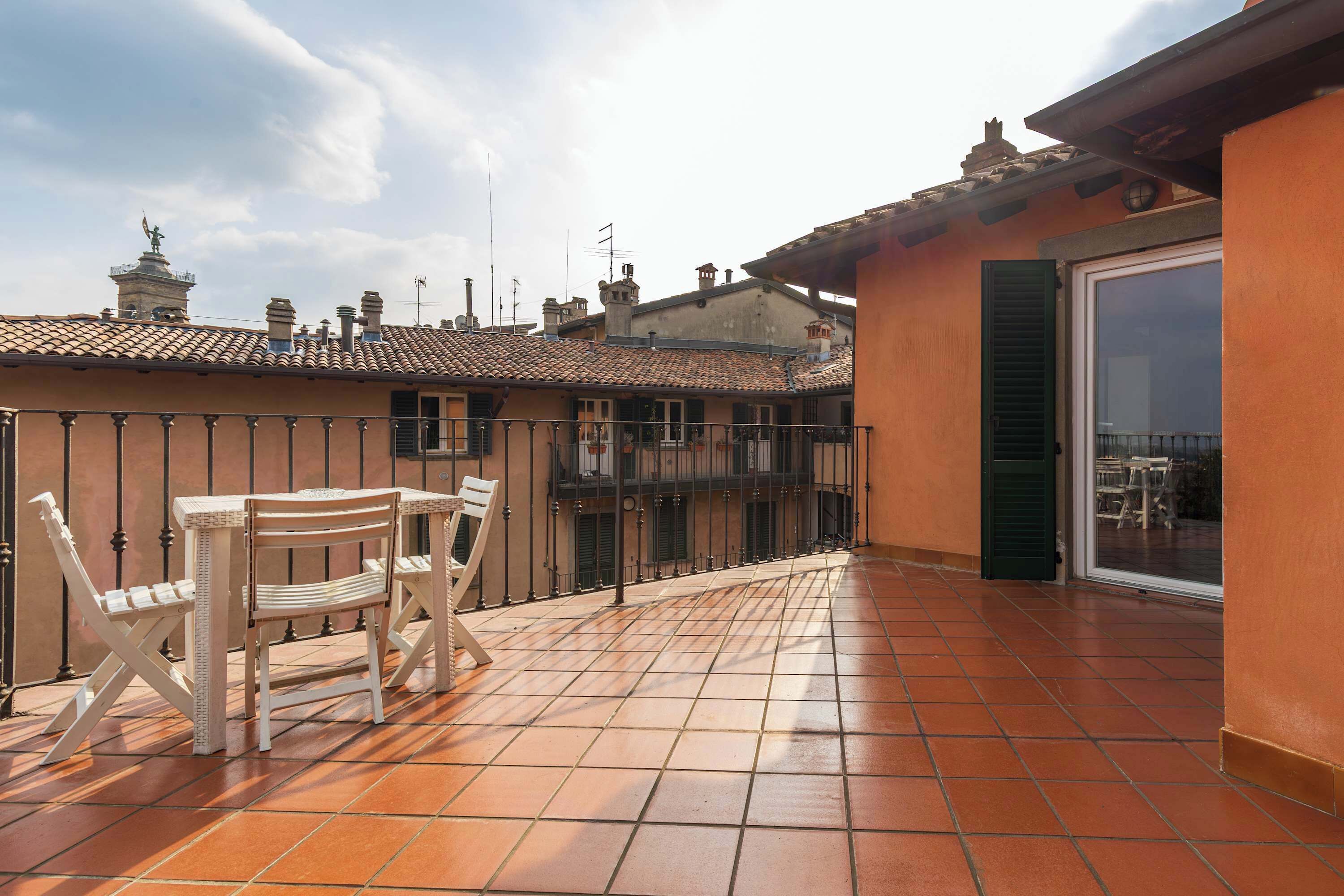 Une terrasse avec une table et des chaises, une vue sur la ville et un bâtiment avec un toit en tuiles.