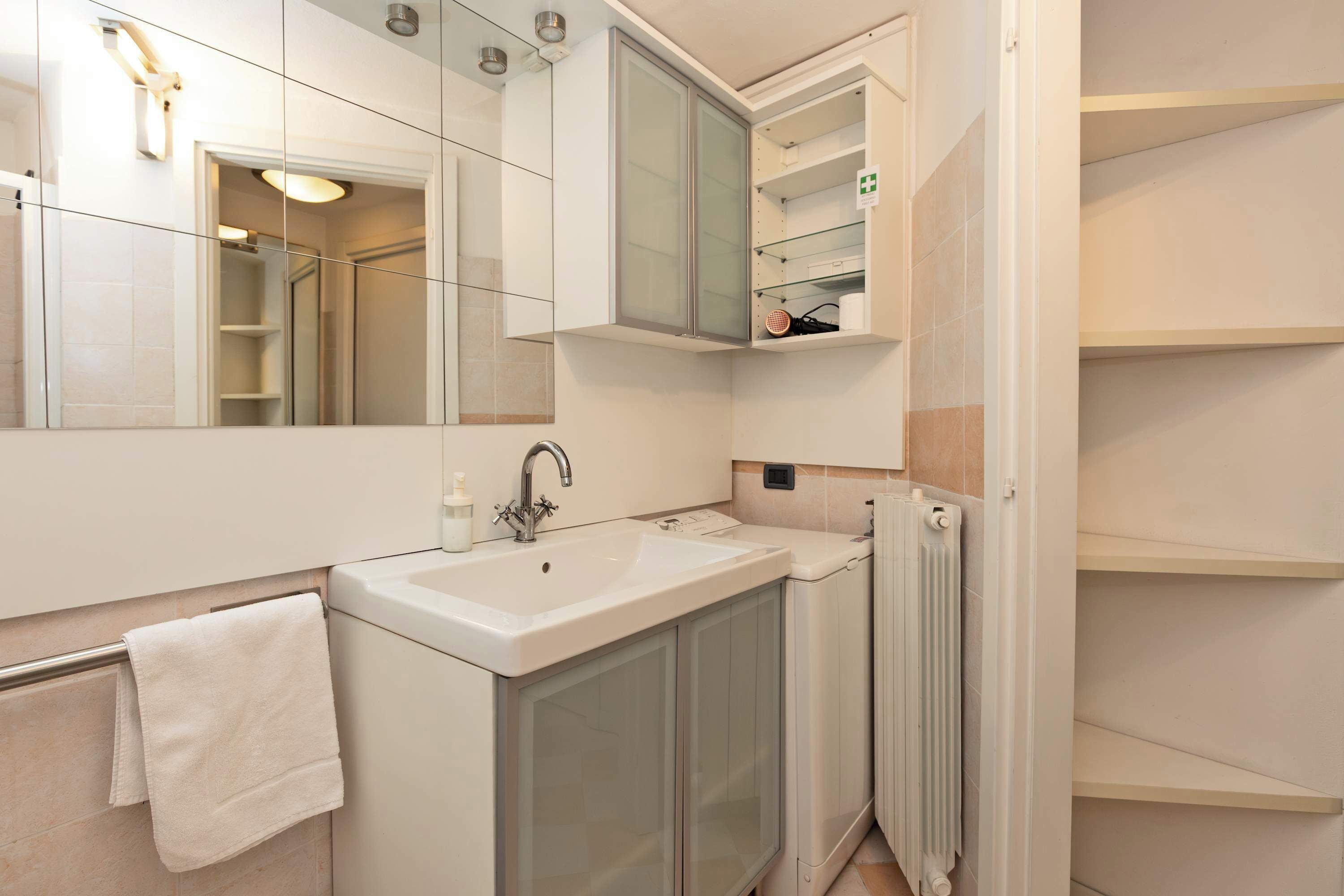 A bathroom with a white sink, a mirror, a towel rack, and a glass cabinet.