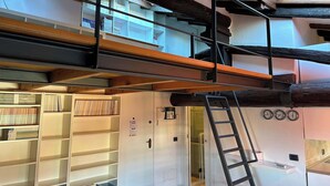 Interior com vários níveis, incluindo uma escada, estantes e uma porta com o número 1.