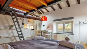 Um quarto com cama, escada, escrivaninha, cadeira, janela e luminária pendente.