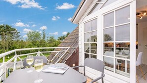 A balcony with a table and chairs, a glass of wine, and a view of the roof and trees. - Syltperle, Germany (Sylt)