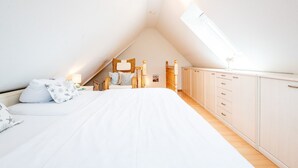 A bedroom with a sloped ceiling, a bed, a wardrobe, and a skylight. - Syltperle, Germany (Sylt)