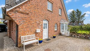 A brick house with a white door, a bench, and a potted plant. - Syltperle, Germany (Sylt)