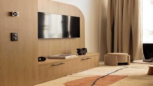 Un salon moderne avec un téléviseur à écran plat fixé à un meuble en bois, un petit pouf et un tapis à motifs.