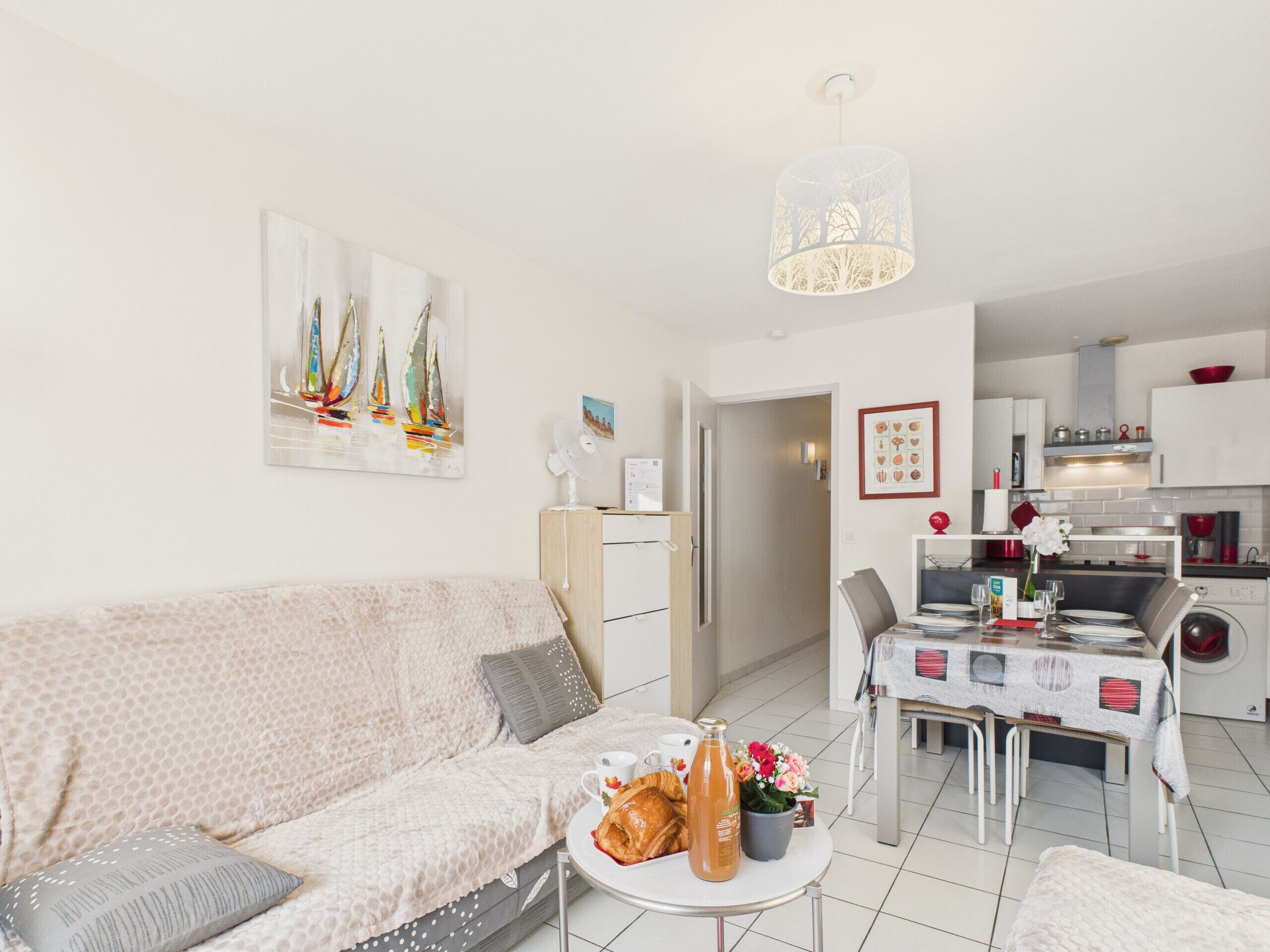 A modern living room with a sofa, a dining table set for two, and a kitchen in the background.