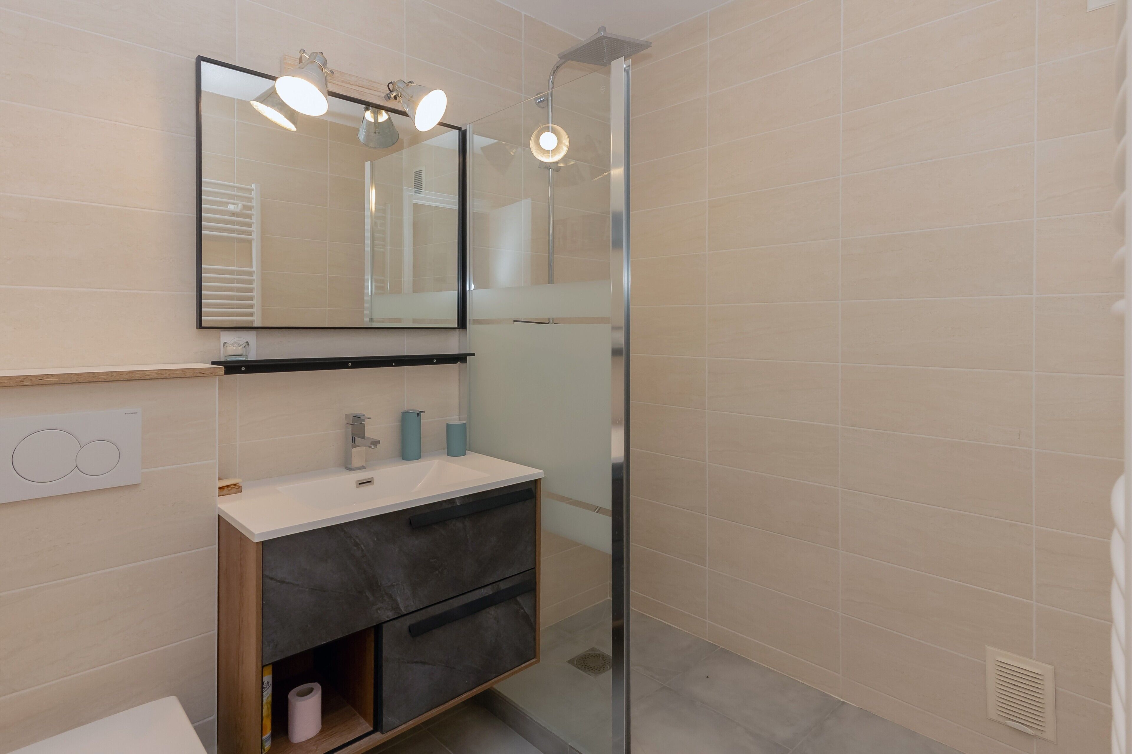 A bathroom with a glass-enclosed shower, a mirror above the sink, and a toilet.