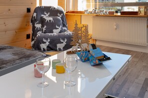A cozy room with a wooden interior, a white table with a glass, a chair with a moose blanket, and a small wooden Christmas tree.
