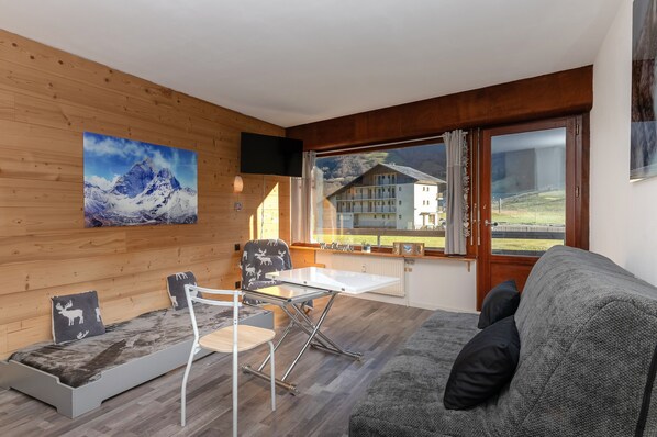 A cozy room with a wooden wall, a sofa, a table, and a chair.