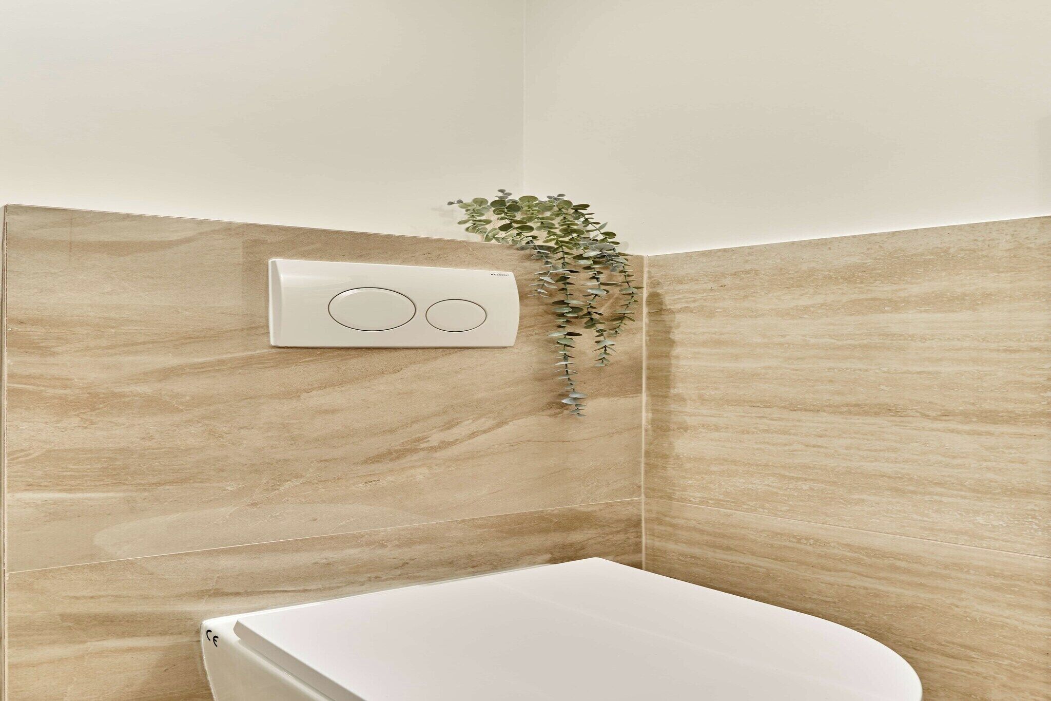 A bathroom with a white toilet, beige marble walls, and a wall-mounted control panel.