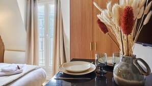 Habitació d'hotel ben ordenada amb un llit, una taula de menjador amb plats i gots, i un ram d'flors seques.