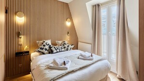 Habitació d'hotel amb un llit, almoines, una taula de nit, una làmpada penjada a la paret i una finestra amb cortines.