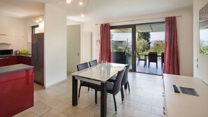 Une cuisine moderne avec un coin repas, une porte-fenêtre coulissante donnant sur un balcon et une vue sur l’extérieur.