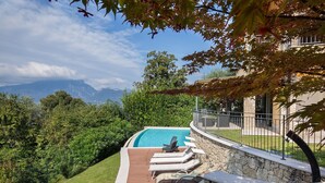 Une piscine entourée de chaises longues, de murs en pierre et offrant une vue sur les montagnes.