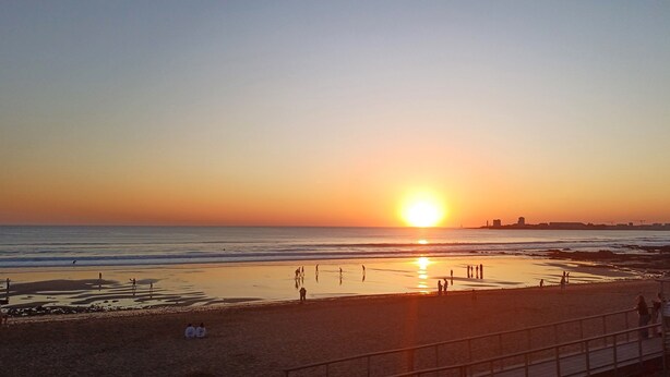 Una spiaggia al tramonto con persone che camminano e siedono sulla sabbia.