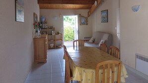 Zona pranzo con tavolo e sedie in legno, angolo cottura con mobili e lavello, e vista sull'esterno.