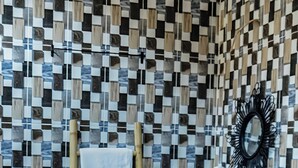 Ein Badezimmer mit Wandpaneelen aus Schachbrettmosaik, einem hölzernen Handtuchhalter, einem weißen Waschbecken und einem schwarzen Spiegel.