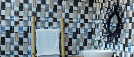 A bathroom with a checkered mosaic wall, a wooden towel rack, a white sink, and a black mirror.