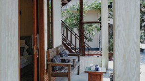 Eine Terrasse im Freien mit einer Holzbank und einem kleinen Tisch, einer Treppe, die zu einer oberen Ebene führt, und Blick ins Grüne.