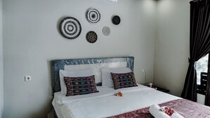 Ein ordentlich bezogenes Bett mit gemusterten Kissen, einem weißen Kopfteil und dekorativer Wandkunst.