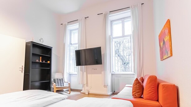 Camera d'albergo con due letti, televisione, armadio, una sedia e finestra con tende.