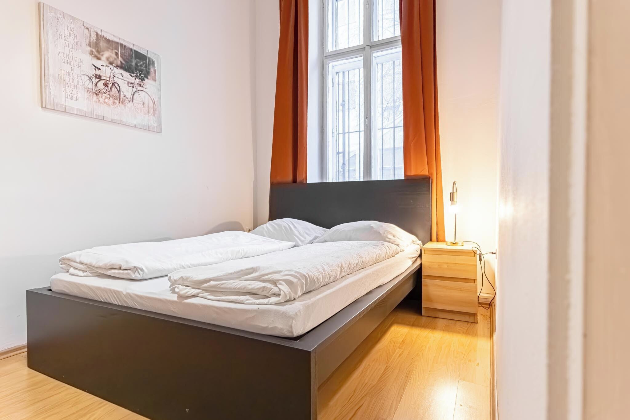 A modern bedroom with a bed, a nightstand, a lamp, and a window with curtains.