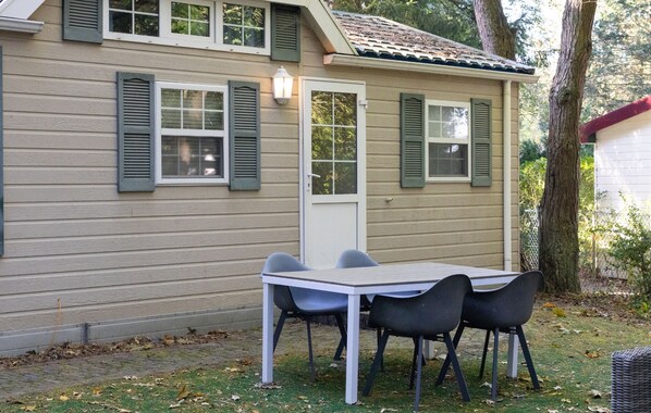 A house with a front door, two windows with shutters, a table with chairs, and a lamp.