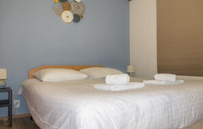 A neatly made bed with white linens and pillows, a bedside table with a lamp, and a wall decoration above the bed.