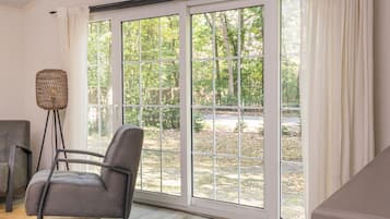 Ein Zimmer mit einer großen Schiebetür, die zu einem Garten führt, ein grau bezogener Sessel und eine Stehlampe.