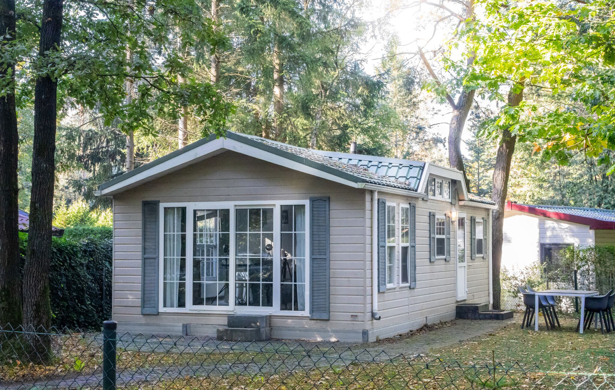 Een klein, gelijkvloers huis met een zadeldak, grote ramen en een omheinde tuin.