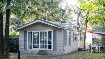 Een klein, gelijkvloers huis met een zadeldak, grote ramen en een omheinde tuin.