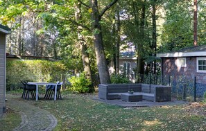 Eine Terrasse mit Gartenmöbeln, einer Backsteinmauer und einem Gartenbereich mit Bäumen.