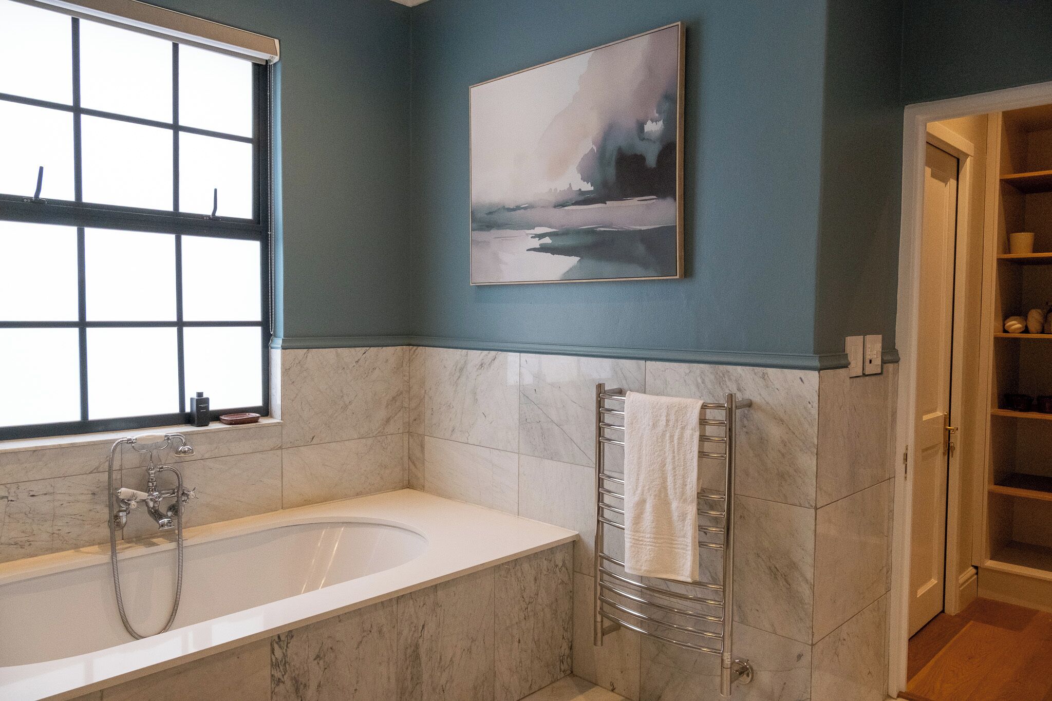 A modern bathroom with a bathtub, a towel rack, and a window.