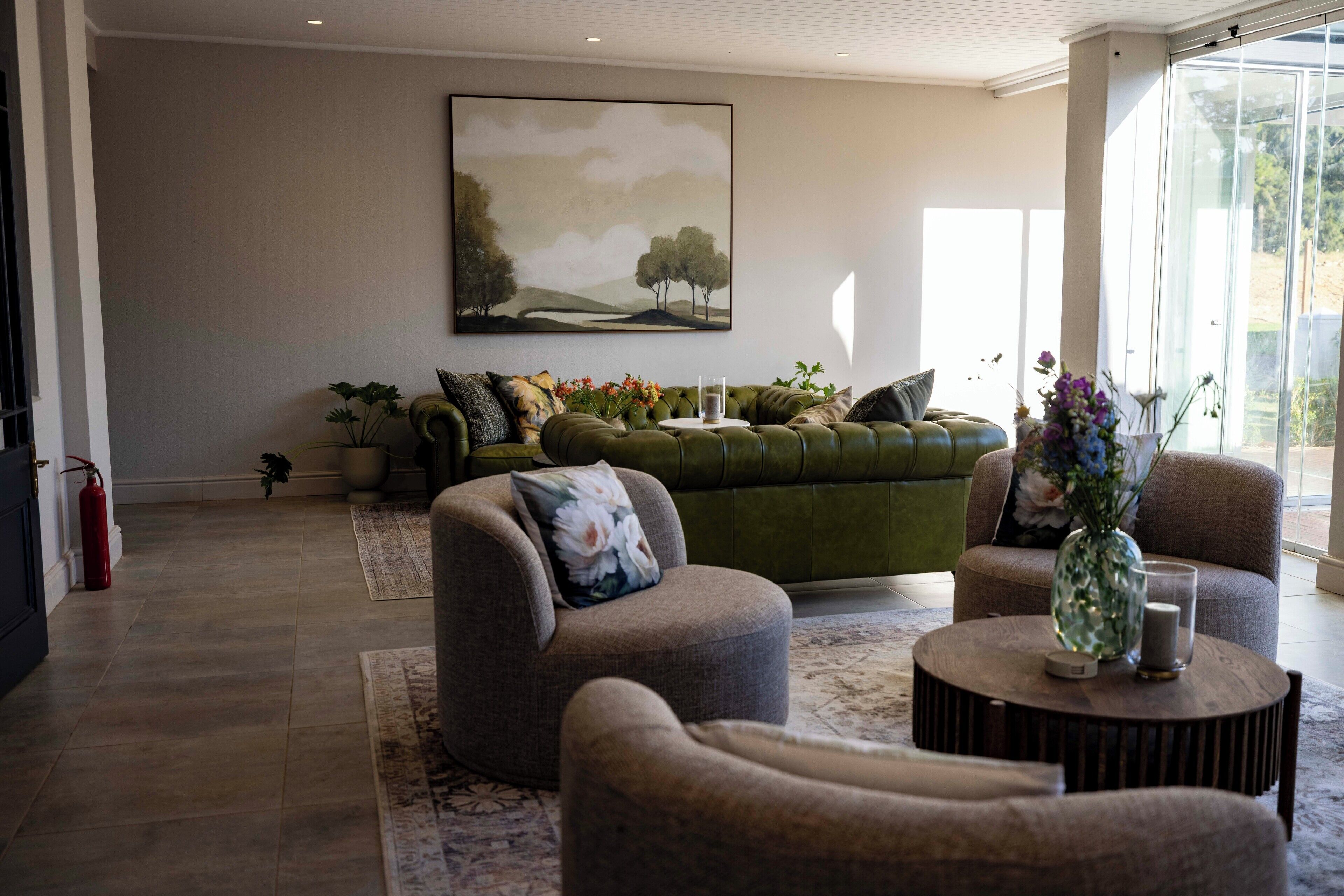 Una sala de estar moderna con un sofá verde, dos sillones y una mesita de centro. Hay un cuadro en la pared y un jarrón con flores sobre la mesita.