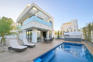 Une maison moderne à deux étages dotée d’une piscine, d’un espace salon extérieur et d’un coin barbecue.