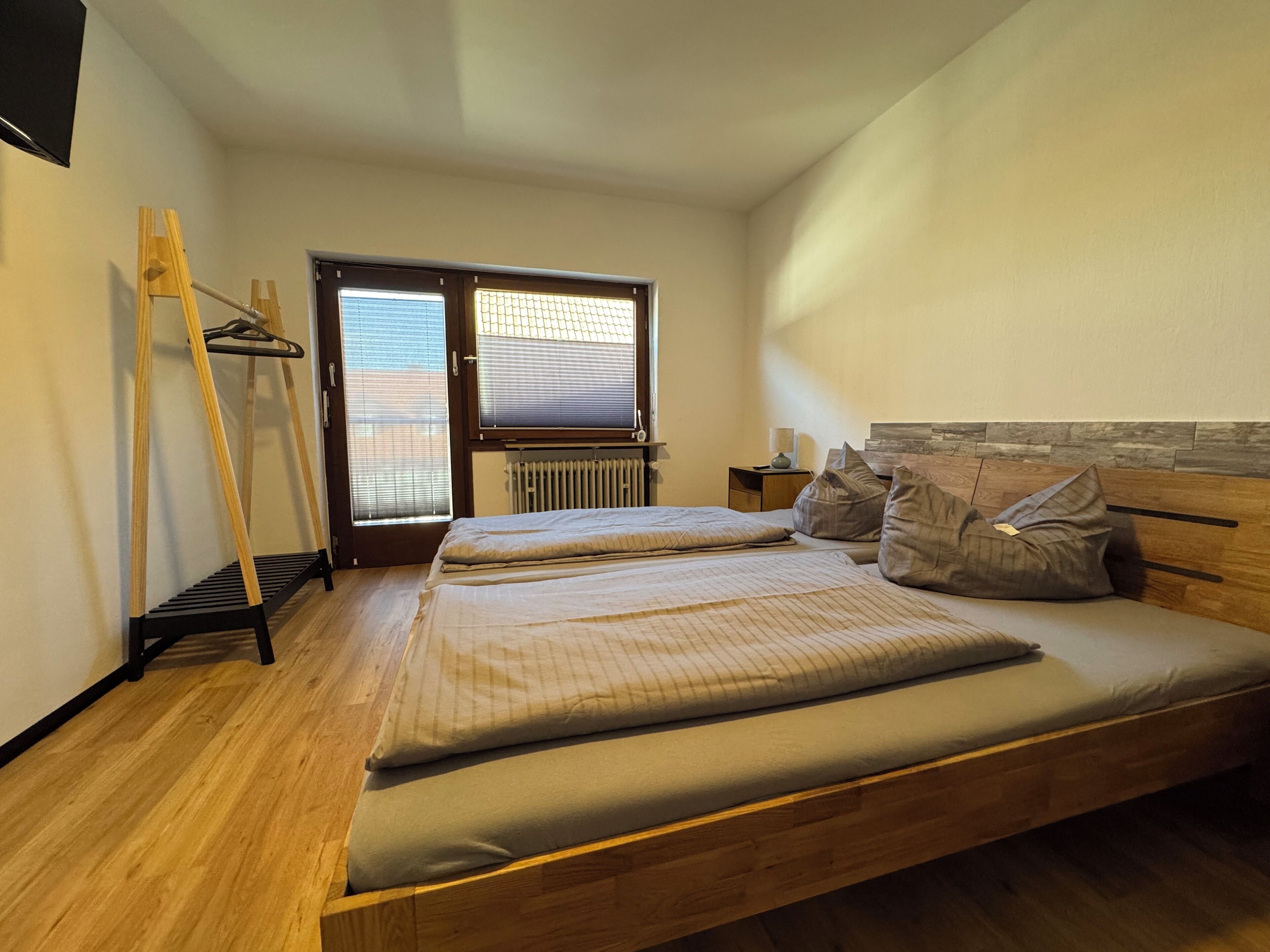 Une chambre avec un lit en bois, une échelle en bois, un radiateur et une fenêtre avec des stores.