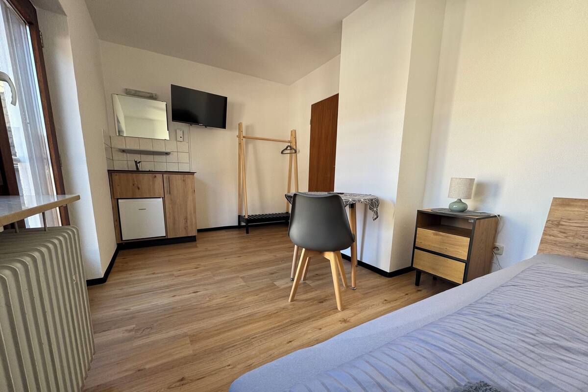 Ett hotellrum med en säng, ett skrivbord, en stol, ett litet bord, en tv och en garderob.