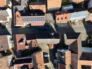 Vista aérea de una zona residencial con varias casas, algunas con paneles solares, una calle con coches aparcados y cielo despejado.