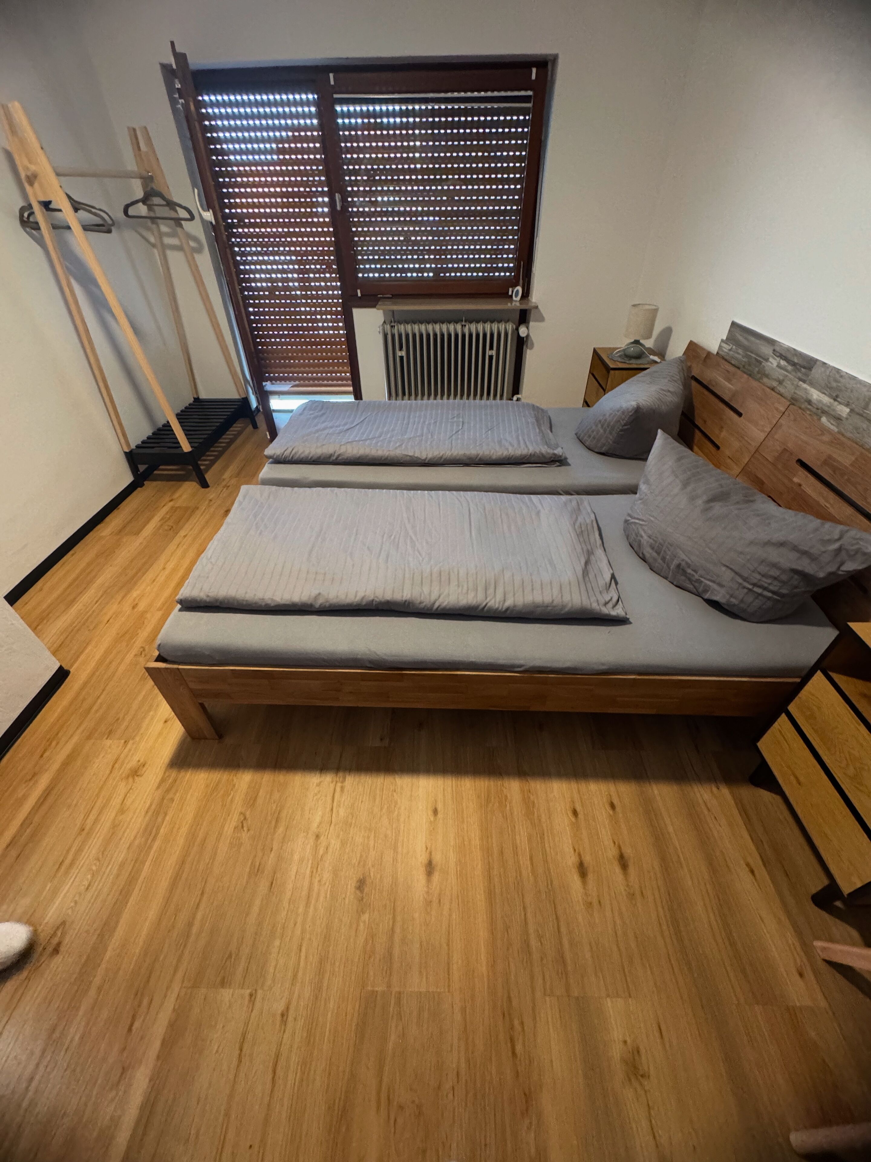 Una habitación con una cama de madera, un radiador, un armario de madera y una ventana con persianas.