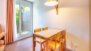 Ein Essbereich mit Holztisch und gelben Stühlen, einer Glastür zum Außenbereich und einer wandmontierten Leuchte.