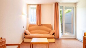 Ein kleiner, gemütlicher Raum mit einer gestreiften Couch, einem kleinen Tisch und einer Glastür, die auf einen Balkon führt.