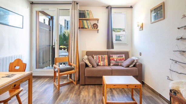 Un salón acogedor con un sofá marrón, sillas de madera, una mesita y una estantería.